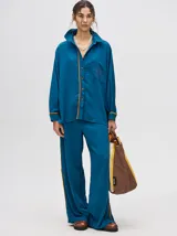 Camisa azul de corte holgado, con cuello camisero, mangas largas con detalles en los puños, bolsillo frontal con bordado y cierre delantero con botones.