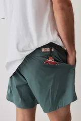 Short de baño color gris oscuro, con cintura elástica ajustable mediante cordones blancos y un pequeño parche decorativo en el borde inferior.
