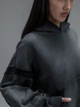 Hoodie oversize de corte crop en color gris oscuro, confeccionado en algodón rústico. Presenta un diseño con costuras expuestas, efecto de desgaste y detalles de roturas en los bordes, incluyendo puños y ruedo.