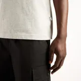 Remera New Balance de hombre, color gris melange, con cuello redondo y parche tejido con logo en el pecho.