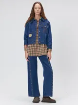 Campera de jean estilo cazadora con corte crop, cierre frontal con botones metálicos, bolsillos delanteros con apliques, bordados y detalles de tachas metálicas en el pecho.