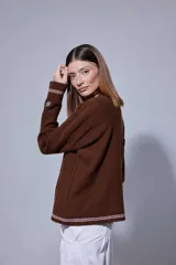 Saco tejido en lambswool con diseño de rombos y trenzas en el frente. Presenta cierre frontal con botones, cuello en V y detalles de rayas en contratono en puños y ruedo. Incluye pin bordado en la manga.