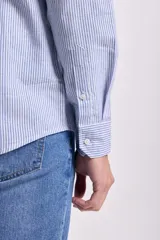 Camisa celeste con rayas verticales blancas, de lino, manga larga y corte clásico.