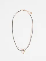 Collar doble compuesto por una cadena fina metálica y un cordón negro, con un dije central de forma ovalada irregular en tono dorado.