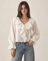 Blusa de algodón tramado color blanco, con escote en V, mangas largas abullonadas con puños elastizados y detalles de volados con encaje en el cuello y frente.