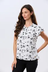 Blusa blanca sin mangas con volados en los hombros, cuello redondo con aberturas y cierre frontal parcial con botones.