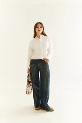 Camisa de corte boxy en color blanco, con cuello clásico, cierre frontal de botones y mangas largas con puños estructurados con tablas. Presenta costuras a contratono y detalle de frunce en la espalda.