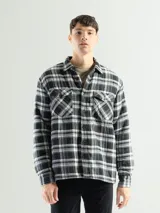 Sobrecamisa de franela a cuadros en tonos negro, gris y blanco, con forro interior de corderito. Presenta cuello clásico, cierre frontal con botones y dos bolsillos con solapa en el pecho.