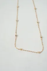 Set de tres collares dorados de diferentes largos y diseños: uno con bolitas espaciadas, otro liso y otro con dijes de flores.