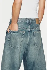Jeans de tiro medio y corte balloon color azul, con trabillas, bolsillos delanteros y traseros, y cierre frontal con cremallera y botón metálico.
