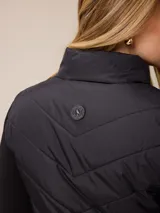 Campera acolchada con frente y espalda en tejido técnico, combinada con mangas y laterales de tejido liso. Presenta cuello alto, cierre frontal completo y bolsillos laterales. Incluye un pequeño detalle bordado en el pecho.