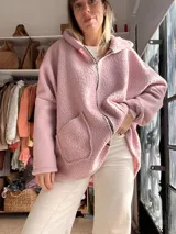 Campera con capucha confeccionada en tejido tipo corderito color rosa, con diseño de patchwork en la espalda que combina parches de tela lisa, texturizada y estampada en tonos verde oliva, marrón y rosa. Presenta un corte holgado y etiqueta de marca en el ruedo.