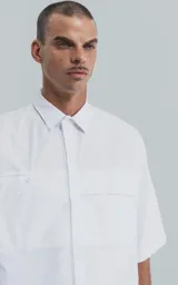 Camisa de manga corta en popelina de algodón, con silueta oversize y diseño funcional que incluye dos bolsillos delanteros, uno de ellos con solapa.