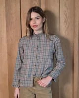 Camisa de algodón con estampado de cuadros en tonos grises y beige. Presenta cuello alto con volados, cierre frontal con botones y mangas largas con puños terminados en volados.