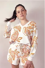 Buzo de cuello en V con mangas largas y puños elásticos, confeccionado en tejido rústico con estampado botánico en tonos rosado y mostaza sobre base blanca.