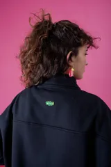 Buzo negro de corte oversize con cuello alto y cierre frontal parcial. Presenta mangas largas, bolsillo tipo canguro delantero y un pequeño detalle bordado en el pecho.