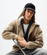 Gorra de estilo aviador con visera curva, confeccionada en poliéster negro. Presenta solapas laterales con forro de piel sintética para cubrir las orejas y ajuste trasero regulable.