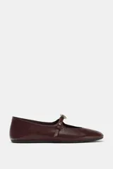 Zapato tipo bailarina de cuero color bordó, con tira ajustable en el empeine, detalle metálico y punta redonda.
