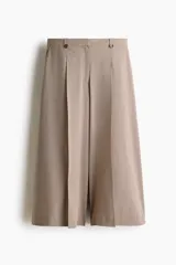 Pantalón sastrero de corte cropped y tiro alto, con piernas amplias y pliegues frontales. Presenta cierre con botón y trabillas en la cintura, en un tono beige con estampado de microcuadros.