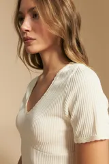 Remera de manga corta en tejido acanalado, con escote en V y detalles de puntilla en el borde del escote y en las mangas. Presenta un ajuste entallado al cuerpo.