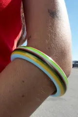 Pack de dos pulseras rígidas de resina, una fina con rayas horizontales multicolores y otra más ancha con rayas verticales multicolores.