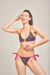 Micro tanga de lycra estampada con palmeras en tonos naranja, amarillo y rosa, con tiras laterales negras para atar.