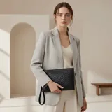 Sobre o clutch negro de eco cuero con diseño tejido en patrón de rombos. Incluye una correa de muñeca desmontable.