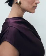 Vestido midi de satén color violeta oscuro, con diseño drapeado en el escote y un hombro al descubierto, de manga corta caída y bajo asimétrico.