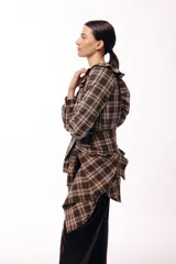 Camisa de manga larga con estampado de cuadros en tonos tierra, cuello redondo y cierre frontal con botones. Presenta volados verticales en el frente y un detalle de lazada en la cintura que permite entallar la prenda.