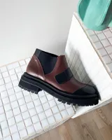 Botas tipo chelsea de cuero vacuno en combinación de colores marrón y negro, con suela track dentada y elásticos laterales.
