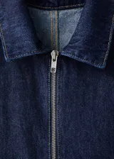 Mono de denim azul oscuro con cierre frontal de cremallera, cuello camisero y mangas cortas. Presenta un corte recto, bolsillos de parche delanteros y traseros, y un cinturón de la misma tela para ajustar la cintura.