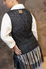 Top tejido a crochet en color dorado con destellos brillantes, de escote redondo y sin mangas. Presenta un diseño de flecos largos en la parte inferior en tonos rojo y dorado.