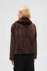 Chaqueta corta de piel sintética en color negro, con cuello clásico, cierre frontal con cremallera y mangas largas.