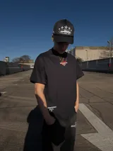 Remera negra de manga corta y corte oversize, con estampa en la espalda que incluye el logo 'IS' en rojo y texto blanco con la leyenda 'ittaidepartament NOT A BRAND, MOVEMENT 04D'.