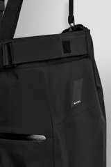 Pantalón deportivo de esquí color negro, confeccionado en tejido técnico impermeable de tres capas con costuras y cremalleras termoselladas. Cuenta con tirantes elásticos regulables, cintura ajustable, bolsillos frontales con cierre, refuerzos en la parte inferior de la pernera y sistema de rescate RECCO integrado.