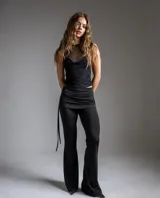 Pantalón largo negro de corte acampanado, tiro bajo, con cintura ancha drapeada y detalles de tiras colgantes en un lateral.