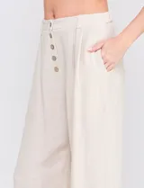 Pantalón palazzo color blanco, confeccionado en mezcla de lino y viscosa, de tiro alto con cierre frontal de botones, pinzas en la cintura y piernas anchas.