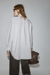 Camisa de corte oversize con cuello solapa, manga larga con puños y bajo asimétrico. Cierre frontal con botones.
