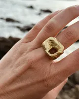 Anillo dorado con forma irregular y un agujero en el centro.