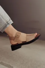 Sandalia de cuero color tostado con tiras anchas, tira en el talón y hebilla metálica rectangular ajustable. Cuenta con suela de goma con tacón bajo y plataforma.