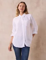 Camisa blanca de lino con cuello con solapa, manga larga regulable con presilla y botón, y abertura central con botones.