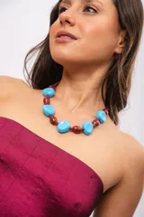 Collar corto compuesto por cuentas circulares de acrílico turquesa intercaladas con cuentas ovaladas de cerámica bordó.