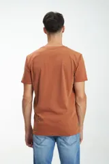 Remera color ladrillo con cuello redondo y manga corta. Presenta un bloque horizontal en el pecho con rayas horizontales en tonos marrón y gris.