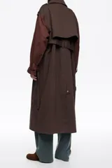 Gabardina de largo medio en color marrón chocolate, con cierre frontal de botones a presión, cuello camisero, mangas largas con puños ajustables, trabillas en hombros y cinturón integrado.
