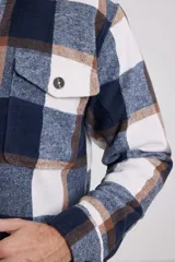 Sobrecamisa de hombre con diseño a cuadros en tonos marrón, beige y blanco. Confeccionada en tejido peludito suave, con cuello clásico, cierre frontal con botones, bolsillo superior y mangas largas con puños abotonados.