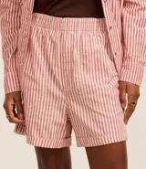 Short tipo runner de sarga color crudo con rayas verticales rojas, cintura elástica y ruedo doblado.