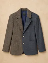 Blazer oversize de diseño bicolor con estructura asimétrica, combinando un lado en color negro y otro en color marrón, ambos con estampado de rayas diplomáticas. Presenta solapas clásicas, cierre frontal con botones de strass y un pin decorativo en forma de perro salchicha.
