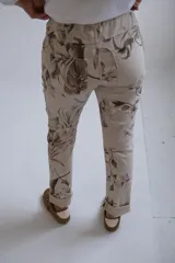 Pantalón de corte recto y ajuste holgado, confeccionado en tela beige con estampado floral en tonos marrones. Presenta cintura elástica con cordón ajustable y ruedos doblados.