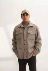 Camisa leñadora de lana fina sin teñir en color tostado, con cuello clásico, cierre frontal de botones, mangas largas con puños abotonados y dos bolsillos delanteros tipo plaqué con solapa.