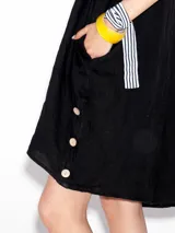 Vestido negro de lino, corte recto, con cuello redondo y mangas cortas. Presenta botones decorativos en la parte inferior.